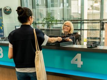 Vrouw wordt geholpen aan een turquoise balie door een glimlachende medewerkster.